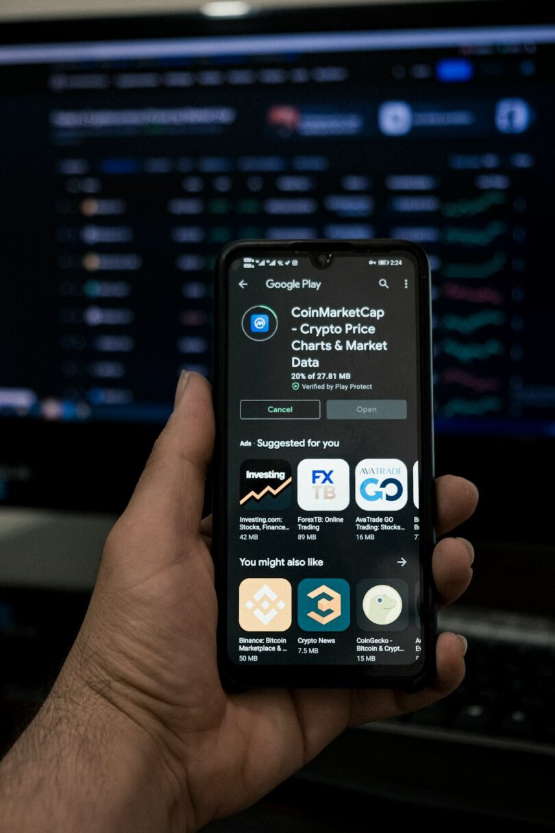 Person using the CoinMarketCap app on a smartphone, with cryptocurrency market data displayed on a background screen